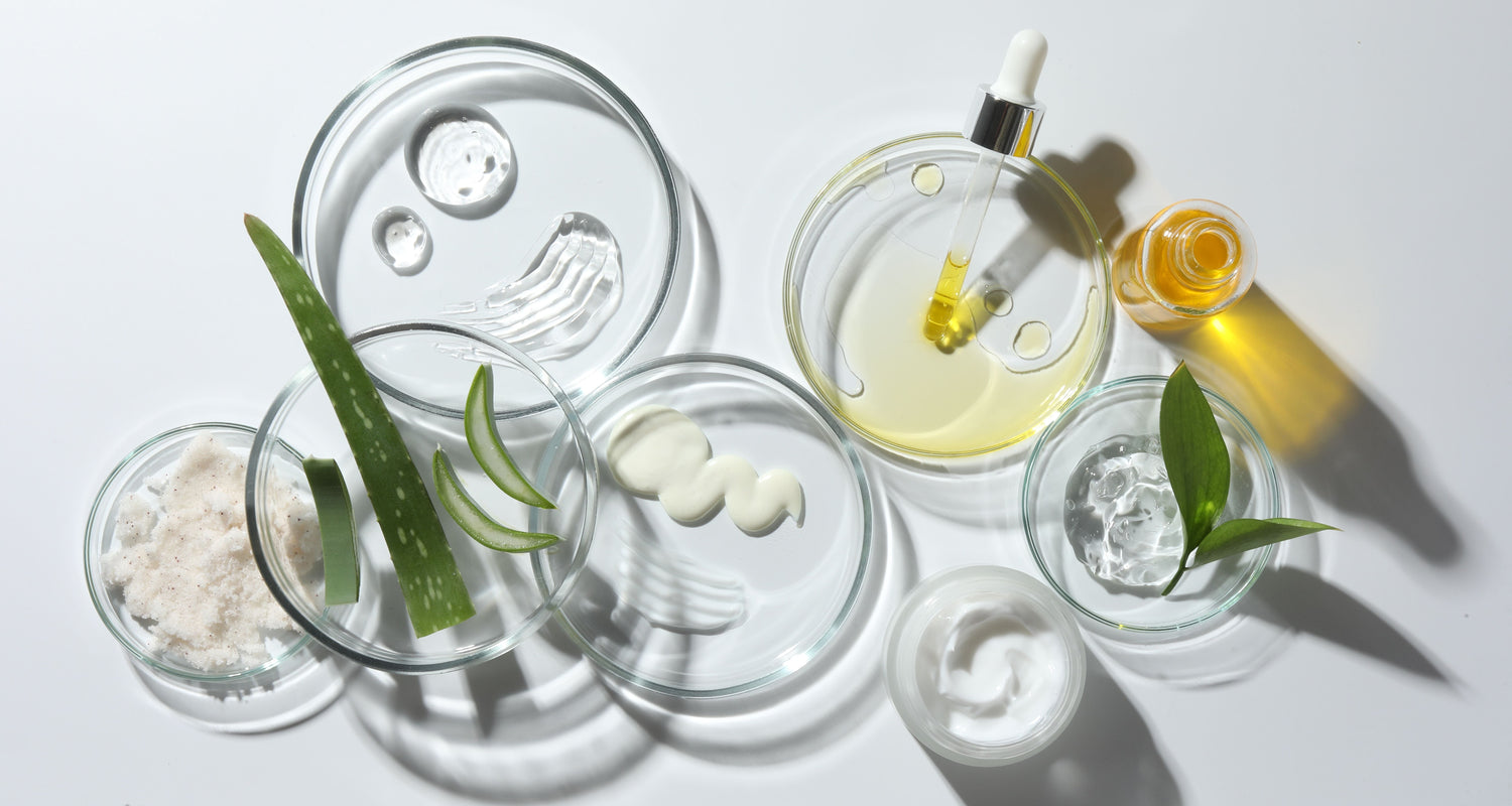 A collection of skincare ingredients in glass bowls, including aloe vera, oils, and creams, arranged on a clean, white surface. The image highlights the purity and simplicity of clean beauty ingredients.