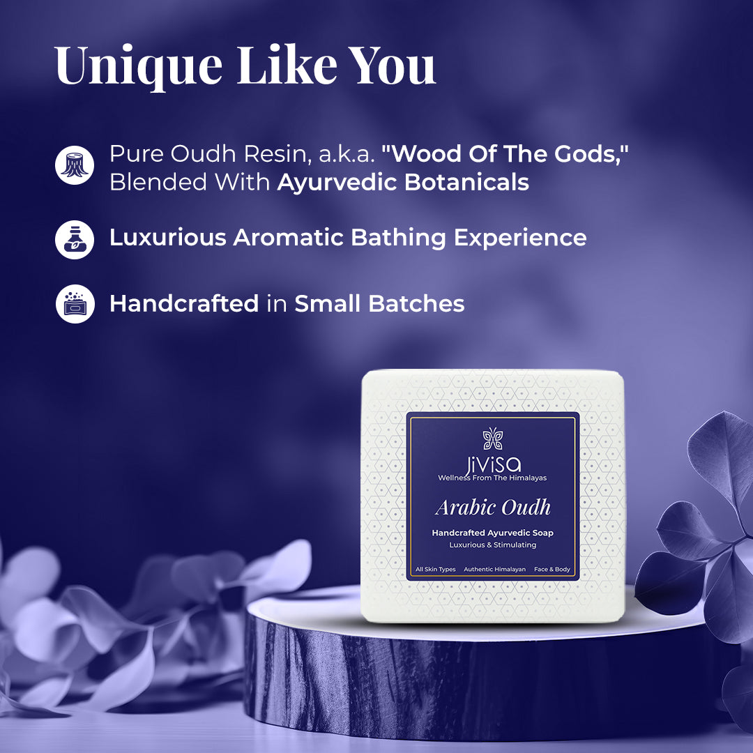 JiViSa Arabic Oudh Handcrafted Ayurvedic Soap bar, in white packaging with a blue and white patterned label, displayed on a circular dark wooden pedestal with purple-toned foliage in the background. Tagline: Unique Like You. Text points: Pure Oudh Resin, a.k.a, "Wood of The Gods," Blended with Ayurvedic Botanicals, Luxurious Aromatic Bathing Experience, and Handcrafted in Small Batches. Product label also shows All Skin Types, Authentic Himalayan, Face & Body, Luxurious & Stimulating.