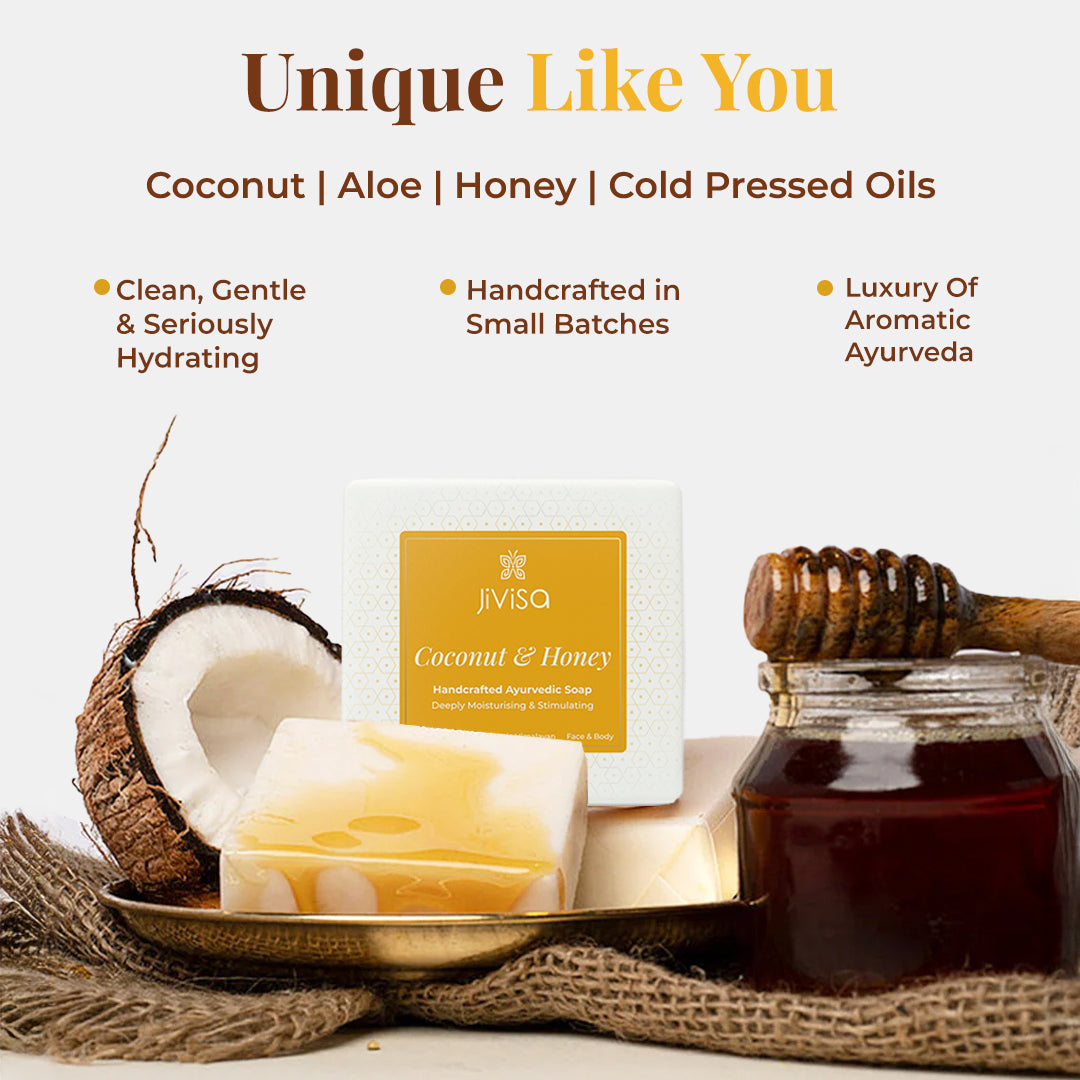 JiViSa Coconut & Honey Handcrafted Ayurvedic Soap bar placed next to its white and gold packaged box. A broken coconut half, a glass jar of honey with a dipper are arranged around it on a textured surface. Tagline: Unique Like You. Key ingredients listed: Coconut | Aloe | Honey | Cold Pressed Oils. Benefits listed: Clean, Gentle & Seriously Hydrating, Handcrafted in Small Batches, Luxury of Aromatic Ayurveda.
