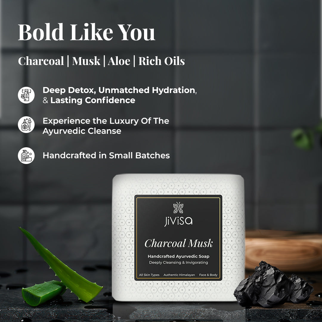 JiViSa Charcoal Musk Handcrafted Ayurvedic Soap bar placed on a dark textured surface with a piece of charcoal and an aloe vera leaf. Tagline: Bold Like You. Text lists key ingredients: Charcoal | Musk | Aloe | Rich Oils. Benefits listed: Deep Detox, Unmatched Hydration, & Lasting Confidence, Experience the Luxury of The Ayurvedic Cleanse, Handcrafted in Small Batches.