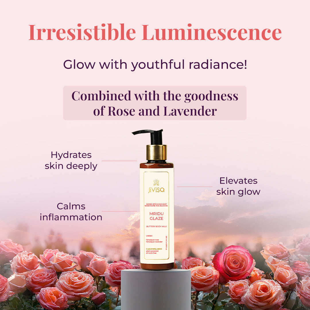 A JiViSa Mridu Glaze Buttery Body Milk bottle stands on a small pedestal, surrounded by lush pink and red roses with water droplets on their petals. Tagline reads "Irresistible Luminescence" followed by the text Glow with youthful radiance below the tagline. The text highlights product ingredients in a pastel color box: Combined with the goodness of Rose and Lavender. Callouts around the bottle indicate benefits: Hydrates skin deeply, Calms inflammation, and Elevates skin glow.
