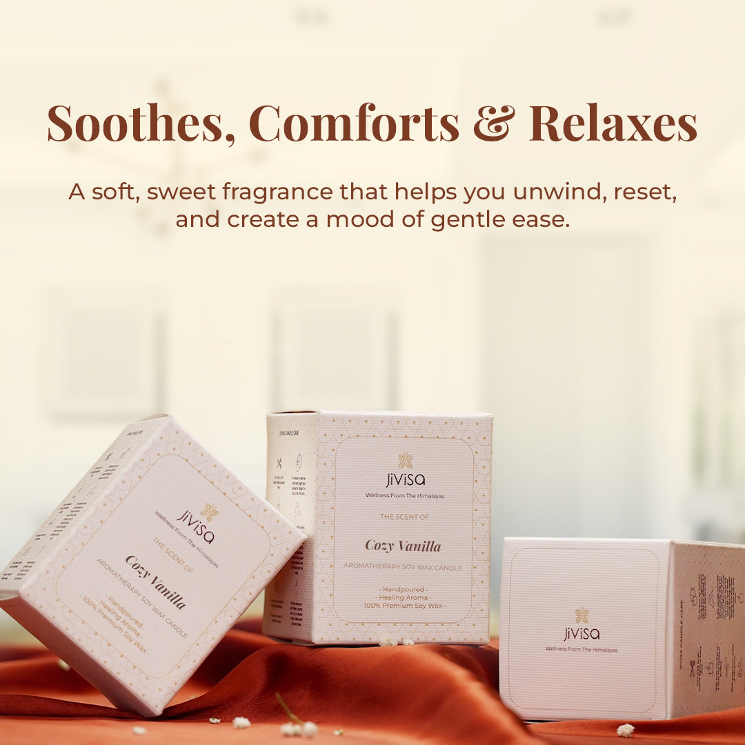 A trio of JiViSa Cozy Vanilla candle boxes is styled on a soft rust-colored fabric, set in a bright room with a blurred background. The headline reads: "Soothes, Comforts & Relaxes," followed by text: "A soft, sweet fragrance that helps you unwind, reset, and create a mood of gentle ease." The boxes are labeled: "JiViSa – The Scent of Cozy Vanilla – Aromatherapy Soy Wax Candle – Handpoured • Healing Aroma • 100% Premium Soy Wax."