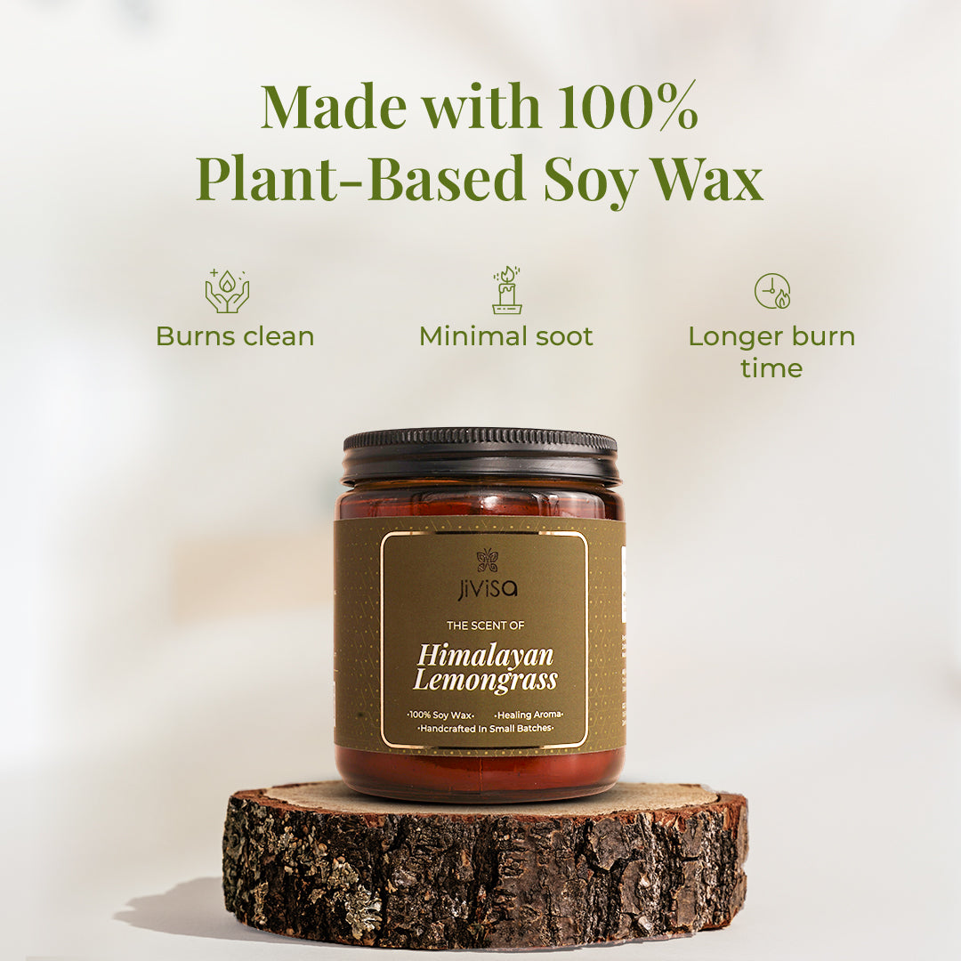 JiViSa Himalayan Lemongrass soy wax candle amber glass jar with black lid sits on a wooden log slice against a minimal background. Above it, bold green text states: "Made with 100% Plant-Based Soy Wax." Three icons highlight key benefits: "Burns clean," "Minimal soot," and "Longer burn time."