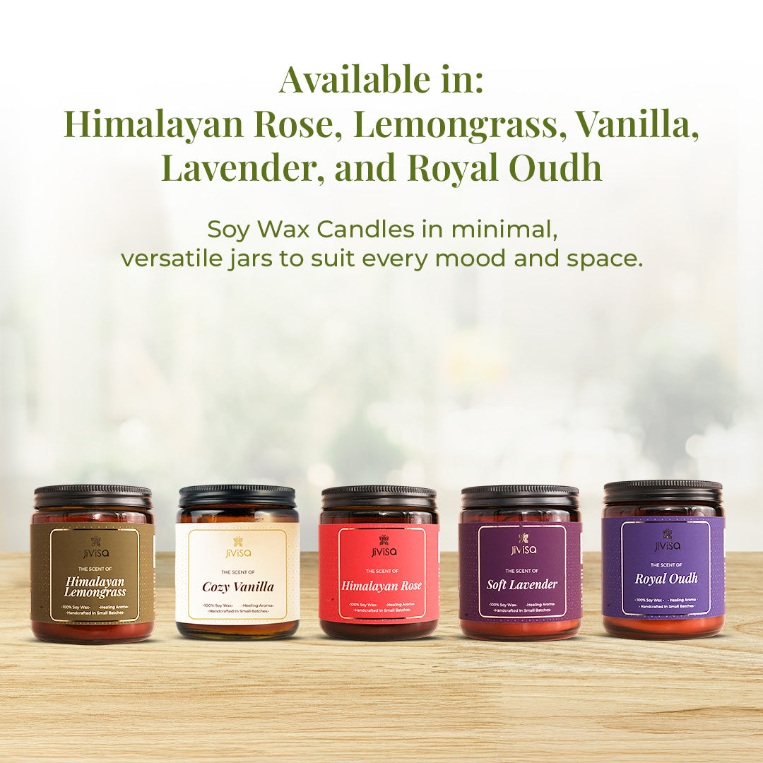 A lineup of five JiViSa soy wax candles placed on a wooden surface with a soft window-lit background. Text above reads: "Available in: Himalayan Rose, Lemongrass, Vanilla, Lavender, and Royal Oudh – Soy Wax Candles in minimal, versatile jars to suit every mood and space."