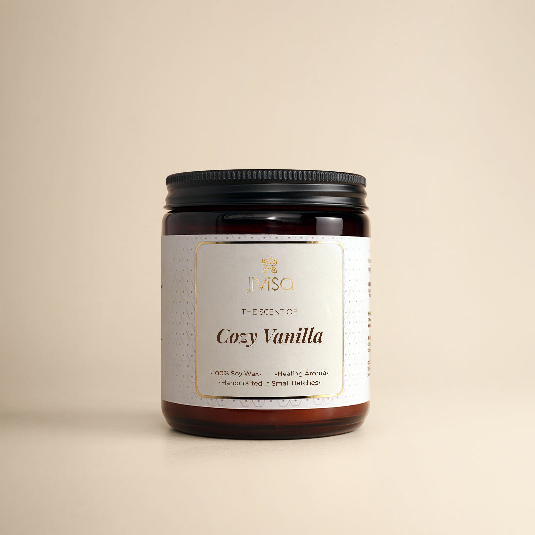 JiViSa Cozy Vanilla soy wax candle in a glossy amber glass jar 180gm with a black lid, placed against a beige background. The label reads: "JiViSa – Wellness From The Himalayas – The Scent of Cozy Vanilla – Handcrafted • 100% Soy Wax • Healing Aroma."