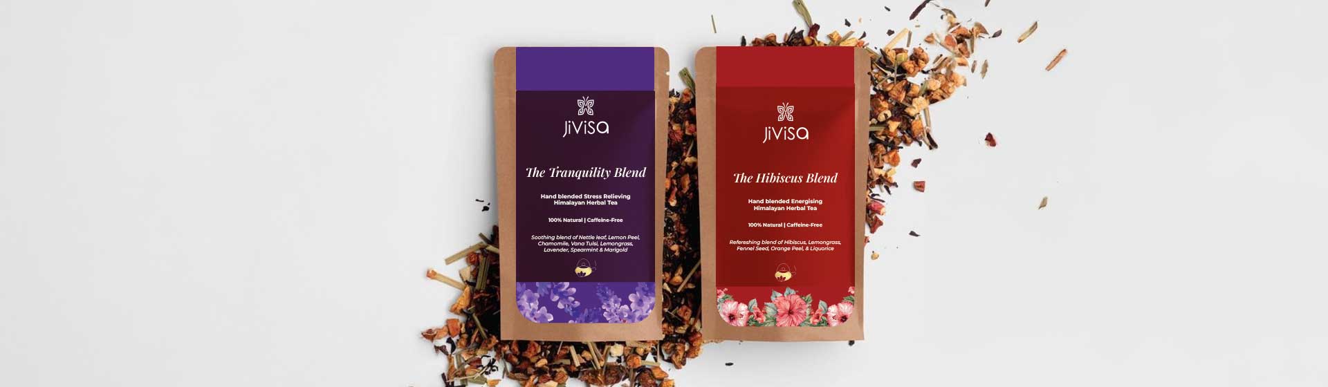 Two JiViSa Himalayan herbal tea packs placed on a scattered bed of loose tea blend over a white background. The left pack is JiViSa Tranquility Blend in a deep purple label, crafted for stress relief with soothing floral illustrations. The right pack is JiViSa Hibiscus Blend in a rich red label, designed for energizing and rejuvenation, decorated with hibiscus flowers. Both are eco-friendly kraft paper pouches labeled as 100% Natural and Caffeine-Free.