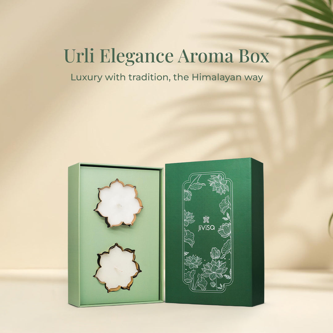 The heading reads: "Urli Elegance Aroma Box- Luxury with tradition, the Himalayan way. An opened JiViSa Urli Elegance Aroma gift box, reveal two white lotus-shaped candles with gold-colored edges inside a pale green insert. The deep green box lid, featuring a white outline of lotus flowers, stands up right next to the open box on a beige background with a hint of green foliage.