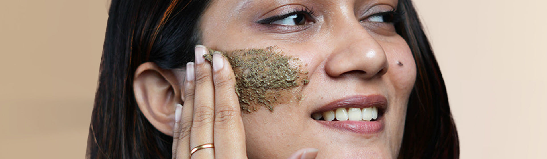 Close up of a woman applying JiViSa Ubtan on her cheek using her fingertips. The herbal face paste has a natural earthy texture, and the close-up shot highlights the gentle exfoliation process and nourishing skincare ritual.