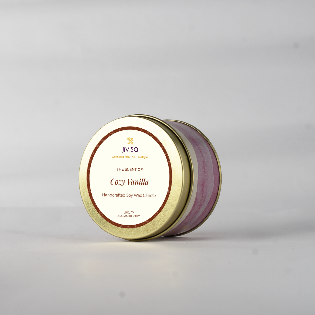 JiViSa Cozy Vanilla handcrafted soy wax candle in a closed gold tin with a decorative pink and white swirl pattern, seen from a slight angle on a plain white background. The label reads: "JiViSa Wellness From The Himalayas, THE SCENT OF Cozy Vanilla, Handcrafted Soy Wax Candle, LUXURY AROMATHERAPY".