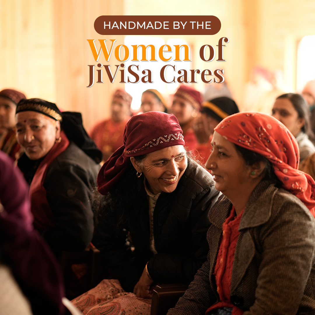 A group of women, appearing to be from the Himalayas are seated and smiling, with one woman in a red head covering looking at another woman and smiling. Text overlay reads: "HANDMADE BY THE Women of JiViSa Cares".
