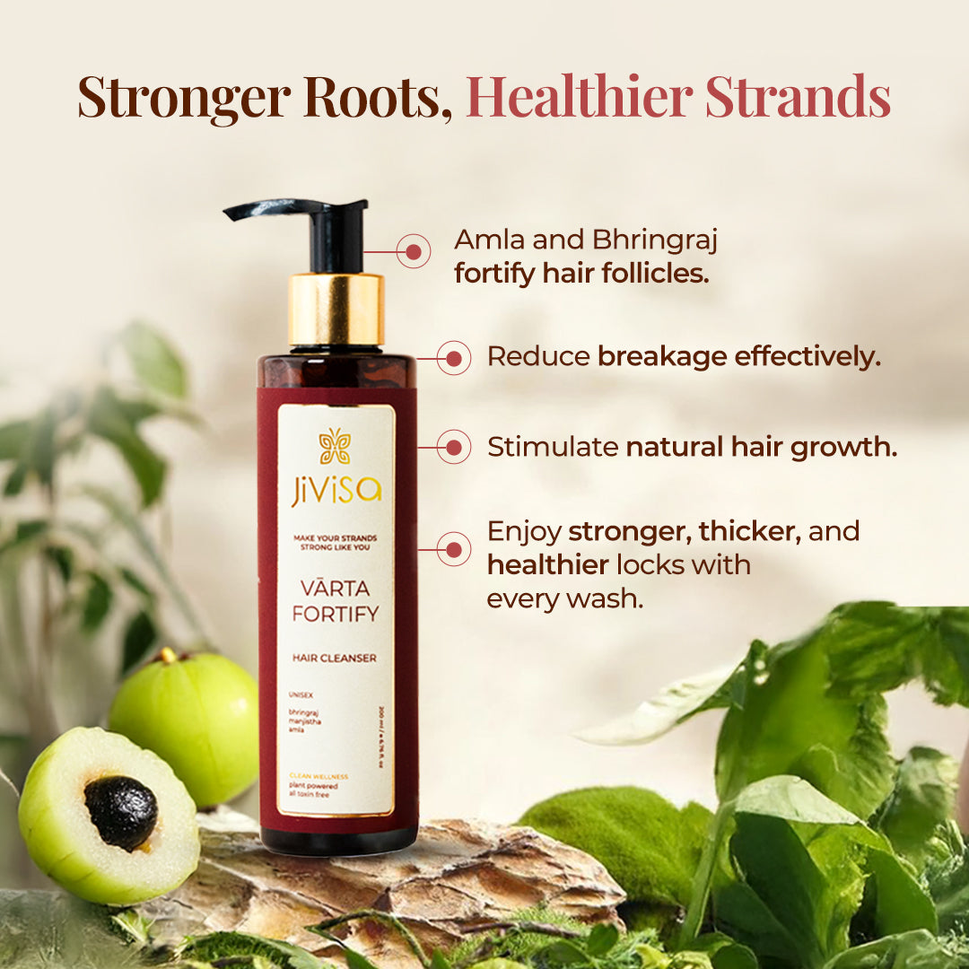 The image features a Bottle of JiViSa-Varta Fortify Hair Cleanser with a pump dispenser is centrally placed, surrounded by its natural ingredients: whole and halved amla fruits, and green Bhringraj leaves. Tagline reads "Stronger Roots, Healthier Strands". The right of the bottle, bullet points highlight the product's benefits: Amla and Bhringraj fortify hair follicles, it reduces breakage effectively, stimulates natural hair growth, and results in stronger, thicker, and healthier locks with every wash.