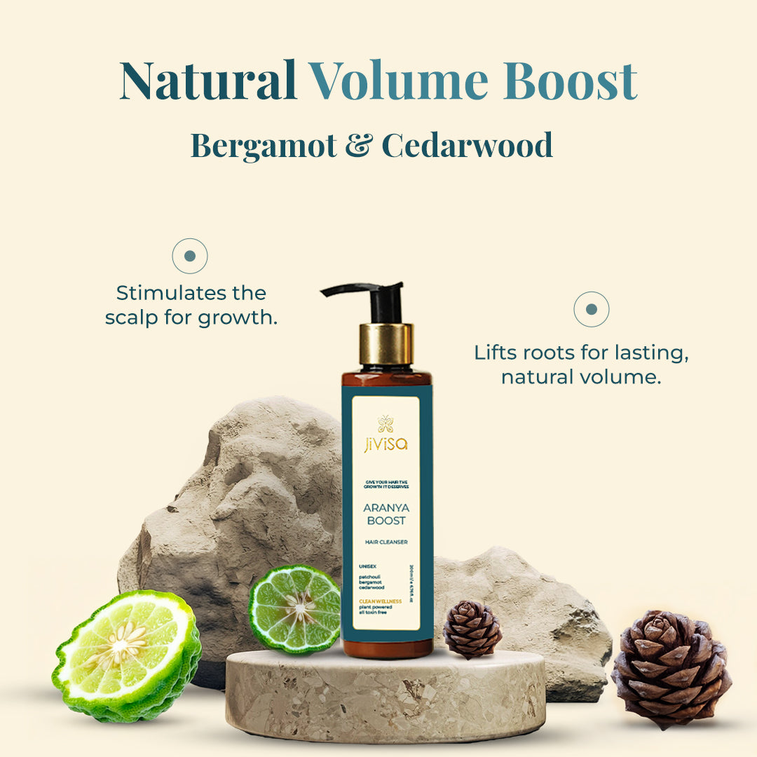 The image showcases JiViSa Aranya Boost Hair Cleanser, Natural Volume Boost Hair Cleanser with Bergamot & Cedarwood. The text highlights that this cleanser stimulates the scalp for growth and lifts roots for lasting, natural volume. The product is presented on a textured stone-like surface, flanked by fresh bergamot fruits and cedarwood cones, emphasizing its natural ingredients. 