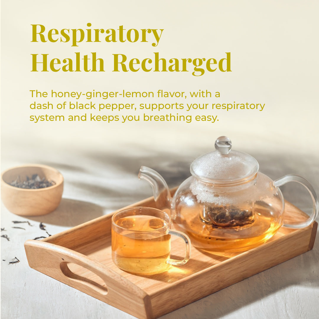 Image showcases a clear glass teapot and a matching cup filled with a light amber JiViSa-the Nectar of Life Immunity Infusion drink, sitting on a wooden tray. The text overlay announces: &quot;Respiratory Health Recharged,&quot; with supporting details: The honey-ginger-lemon flavor, with a dash of black pepper, supports your respiratory system and keeps you breathing easy.  A small wooden bowl with dark tea leaves is visible in the background.
