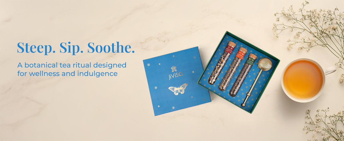Steep. Sip. Soothe. – A botanical tea ritual designed for wellness and indulgence. JiViSa Botanical Brew tea gift box with three glass tubes of botanical tea blends and a golden tea infuser, placed beside a cup of tea and white flowers on a marble background.