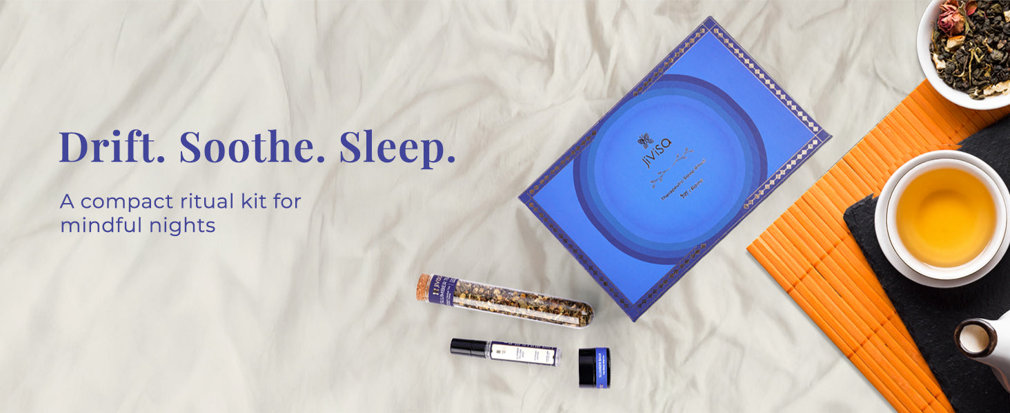 A JiViSa Raina Sleep Ritual Kit is displayed on a soft, wrinkled white cloth. The kit includes a luxury blue box with a concentric circle design, a small clear tube of tranquility tea leaves, a pillow mist roller bottle, and a sleep balm. A clear glass mug of prepared tea and a small bowl of loose tea leaves are also visible. The text on the image reads, "Drift. Soothe. Sleep," with a sub-headline: "A compact ritual kit for mindful nights."