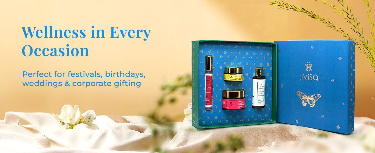 An open JiViSa Self Care Bloom Gift Box is showcased, revealing four products: Tarang Glaze Body Milk, Rose Drench Face and Body Mist, Haridra Quench Healing Aloe Gel, and Desi Gulaab Clay Masque. The heading on the image reads "Wellness in Every Occasion," followed by the subheading "Perfect for festivals, birthdays, weddings & corporate gifting." The background features soft, warm tones with blurred greenery and a draped white fabric.