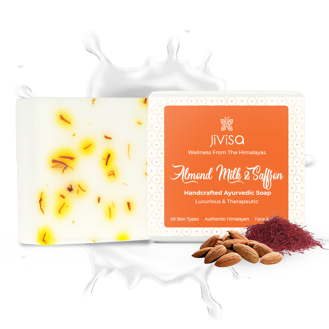 Image features the JiViSa Almond Milk &amp; Saffron Handcrafted Ayurvedic Soap with a milk splash effect, emphasizing hydration and richness and saffron threads &amp; Almonds shown alongside its packaging scattered at the bottom. The packaging clearly labels it as &quot;Luxurious &amp; Therapeutic&quot; and suitable for All Skin Types and Face &amp; Body.
