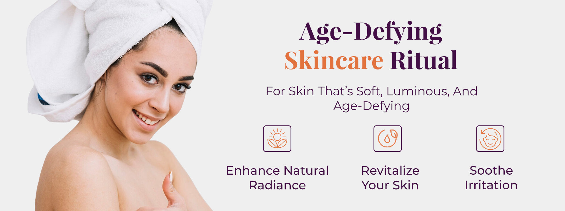 A woman with a towel wrapped around her head smiles and gives a thumb-up. On the right side of the image, the headline reads, “Age-Defying Skincare Ritual” followed by the subtext 'For Skin That’s Soft, Luminous, And Age-Defying.' Below this, three icons are labeled “Enhance Natural Radiance,” “Revitalize Your Skin,” and “Soothe Irritation.” 