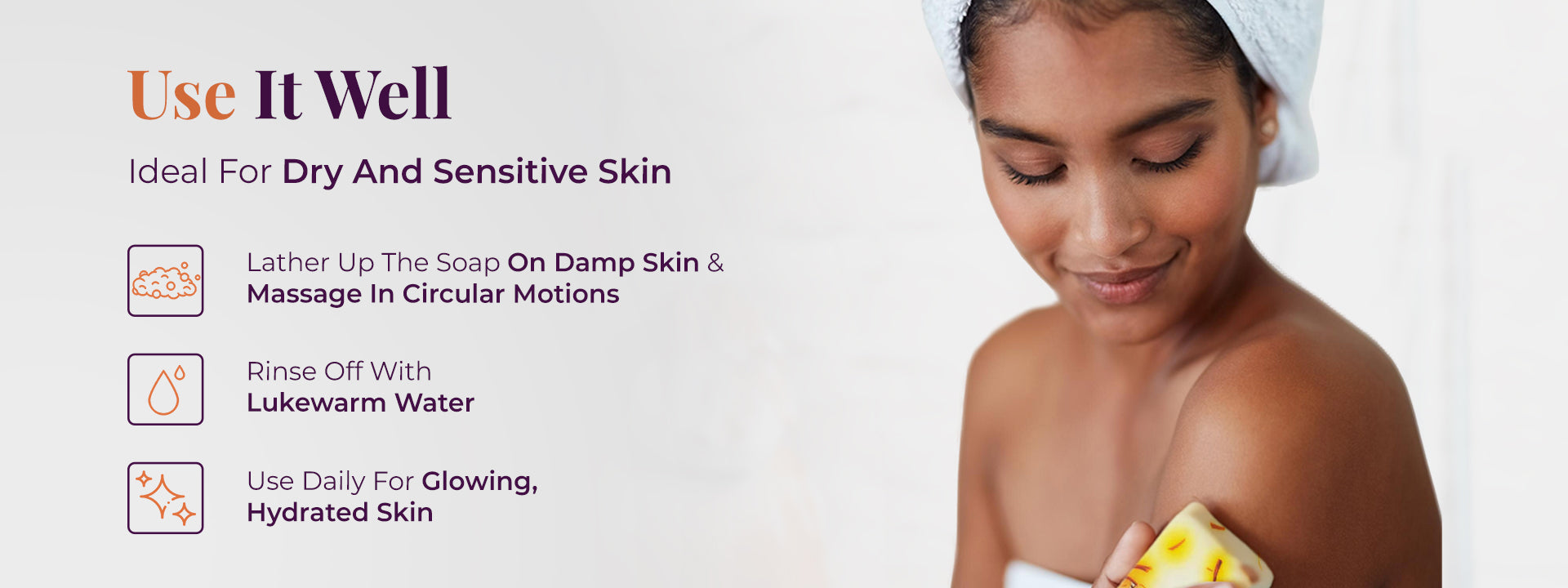 A woman with a towel on her head gently applies JiViSa Almond Milk & Saffron Ayurvedic soap bar with visible saffron strands to her shoulder. The headline reads “Use It Well,” with the subtext “Ideal For Dry And Sensitive Skin.” Three steps are listed alongside icons: “Lather Up The Soap On Damp Skin & Massage In Circular Motions,” “Rinse Off With Lukewarm Water,” and “Use Daily For Glowing, Hydrated Skin.” The visual guides the user on basic application steps.