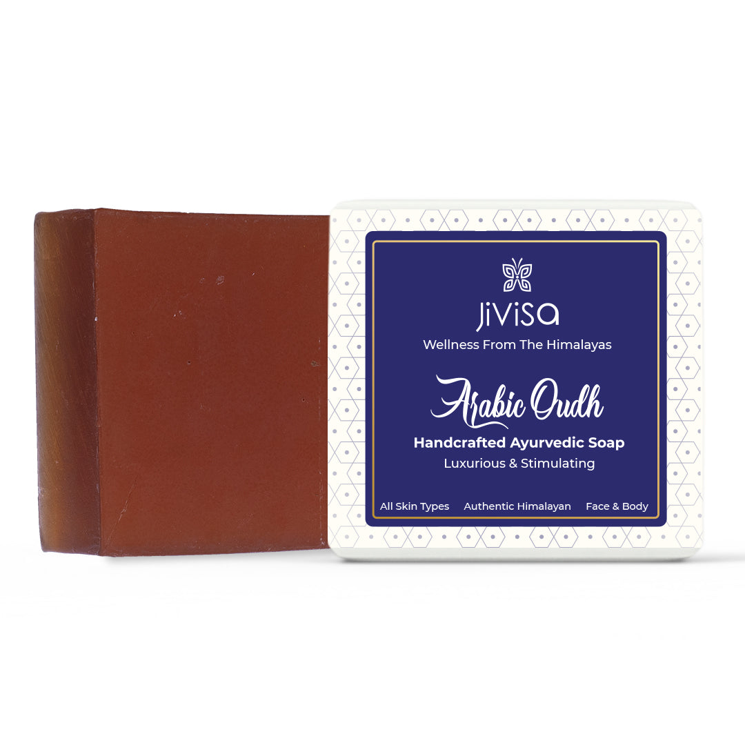 A deep brown JiViSa Arabic Oudh Handcrafted Ayurvedic Soap bar is placed beside its packaging box with a blue and white patterned label. The label reads: JiViSa – Wellness From The Himalayas-Arabic Oudh Handcrafted Ayurvedic Soap, Luxurious &amp; Stimulating with notes: &