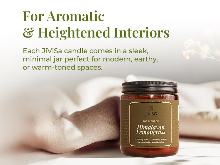 JiViSa Himalayan Lemongrass soy wax candle amber jar is displayed on a soft, neutral-toned surface with delicate pink flowers in the background. The text on the left reads: “For Aromatic & Heightened Interiors.” Below it, the description states: “Each JiViSa candle comes in a sleek, minimal jar perfect for modern, earthy, or warm-toned spaces.” The overall aesthetic is calm, warm, and minimal.