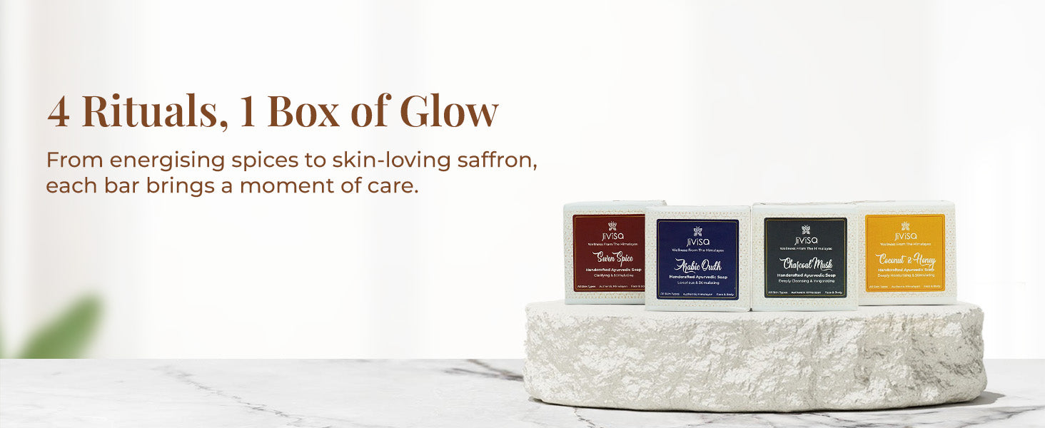 Tagline reads: "4 Rituals, 1 Box of Glow" followed by a text describe JiViSa soap key feature "From energising spices to skin-loving saffron, each bar brings a moment of care". Display of four variants of JiViSa Handcrafted Ayurvedic soap bars: Seven Spice, Arabic Oudh, Charcoal Musk, and Coconut & Honey arranged on a textured white stone pedestal.

