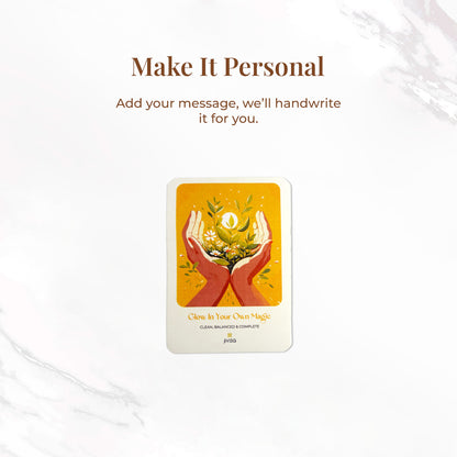 &quot;Make it personal – We’ll handwrite your message for you.&quot; A handwritten card with warm yellow and orange tones shows two hands holding blooming herbs with a glowing sun. Placed on a white surface, the image emphasizes the personal, heartfelt gifting experience JiViSa offers.