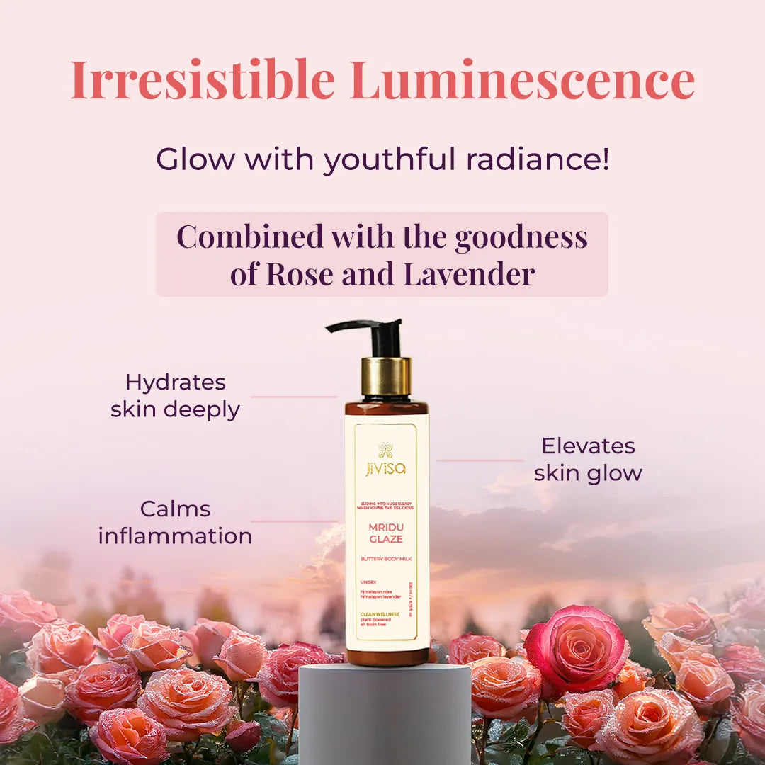 A JiViSa Mridu Glaze Buttery Body Milk bottle stands on a small pedestal, surrounded by lush pink and red roses with water droplets on their petals. Tagline reads "Irresistible Luminescence" followed by the text Glow with youthful radiance below the tagline. The text highlights product ingredients in a pastel color box: Combined with the goodness of Rose and Lavender. Callouts around the bottle indicate benefits: Hydrates skin deeply, Calms inflammation, and Elevates skin glow.