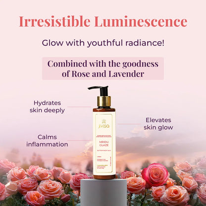 A JiViSa Mridu Glaze Buttery Body Milk bottle stands on a small pedestal, surrounded by lush pink and red roses with water droplets on their petals. Tagline reads "Irresistible Luminescence" followed by the text Glow with youthful radiance below the tagline. The text highlights product ingredients in a pastel color box: Combined with the goodness of Rose and Lavender. Callouts around the bottle indicate benefits: Hydrates skin deeply, Calms inflammation, and Elevates skin glow.