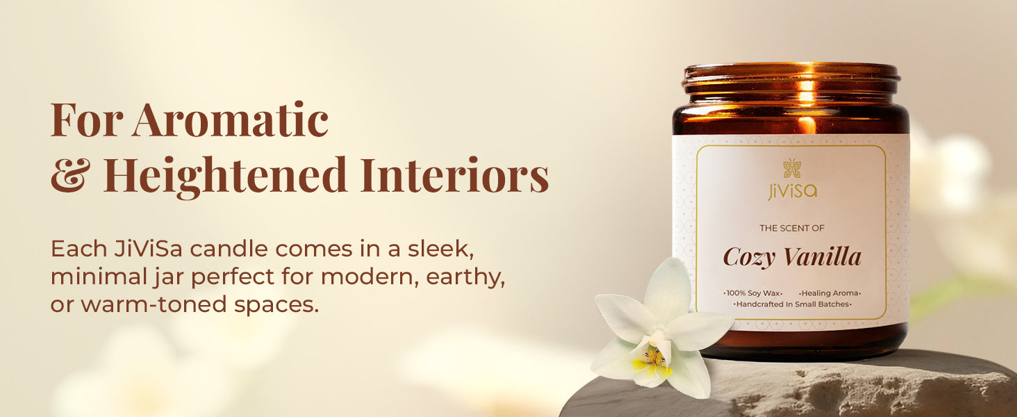 A premium brown glass candle jar labeled "JiViSa – The Scent of Cozy Vanilla" is placed on a natural stone surface with a delicate white flower beside it. The background is a soft beige, conveying a warm, luxurious interior vibe. The tagline on the image reads: "For Aromatic & Heightened Interiors," followed by the text: "Each JiViSa candle comes in a sleek, minimal jar perfect for modern, earthy, or warm-toned spaces."