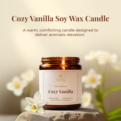  JiViSa Cozy Vanilla candle placed on a stone surface with white vanilla flowers in the background. The tagline above reads: &quot;Cozy Vanilla Soy Wax Candle – A warm, comforting candle designed to deliver aromatic elevation.&quot; The label on the jar reads: &quot;The Scent of Cozy Vanilla – 100% Soy Wax • Healing Aroma • Handcrafted In Small Batches.&quot;