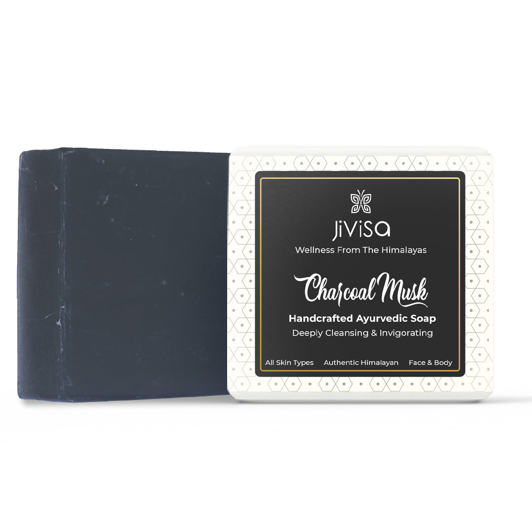 JiViSa Charcoal Musk Handcrafted Ayurvedic Black Colored Soap bar, placed beside to its white and black packaging box. The front label reads: “JiViSa – Wellness From The Himalayas-Charcoal Musk Handcrafted Ayurvedic Soap&quot;. Followed by subtext &