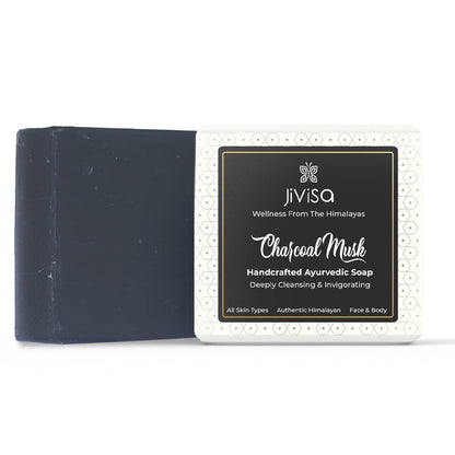JiViSa Charcoal Musk Handcrafted Ayurvedic Black Colored Soap bar, placed beside to its white and black packaging box. The front label reads: “JiViSa – Wellness From The Himalayas-Charcoal Musk Handcrafted Ayurvedic Soap&quot;. Followed by subtext &