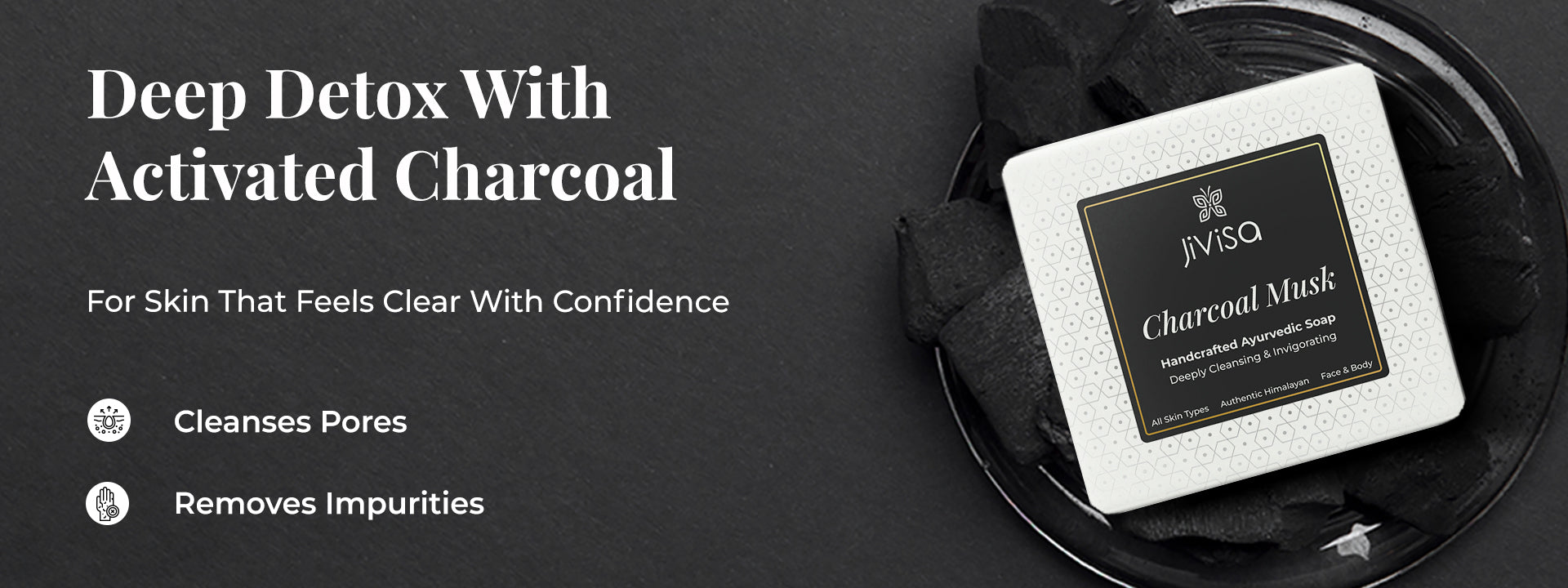 Top view of JiViSa Charcoal Musk Ayurvedic Handmade Soap placed on black charcoal; heading reads “Deep Detox With Activated Charcoal”; subtext: 'For skin that feels clear with confidence'; two icons below highlight: “Cleanses Pores” and “Removes Impurities.”