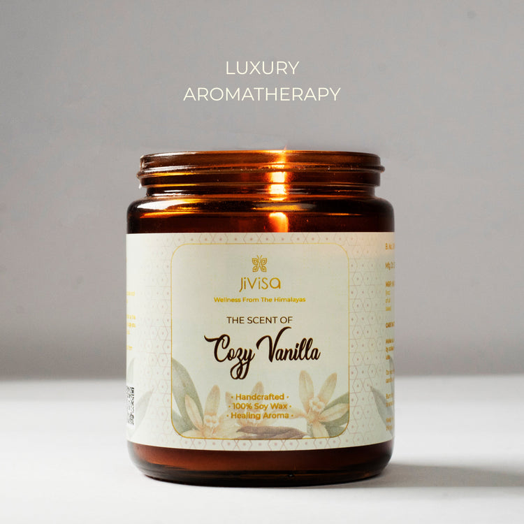 JiViSa Cozy Vanilla soy wax candle in a glossy amber glass jar against a clean grey background. The candle label reads: "JiViSa – Wellness From The Himalayas – The Scent of Cozy Vanilla – Handcrafted • 100% Soy Wax • Healing Aroma." Above the jar, the text "Luxury Aromatherapy" is displayed, emphasizing the premium sensory experience.