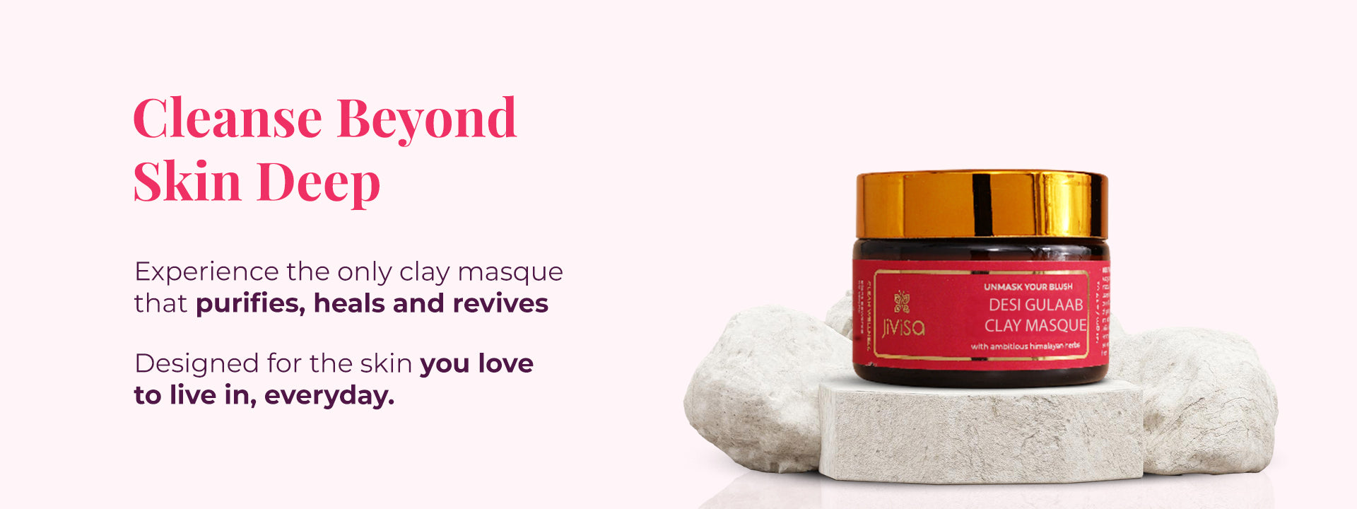 JiViSa Desi Gulaab Clay Masque in a dark jar with a red label and gold lid, resting on two white rocks on a light pink background. To the left, text reads: "Cleanse Beyond Skin Deep". Experience the only clay masque that purifies, heals and revives. Designed for the skin you love to live in every day. 