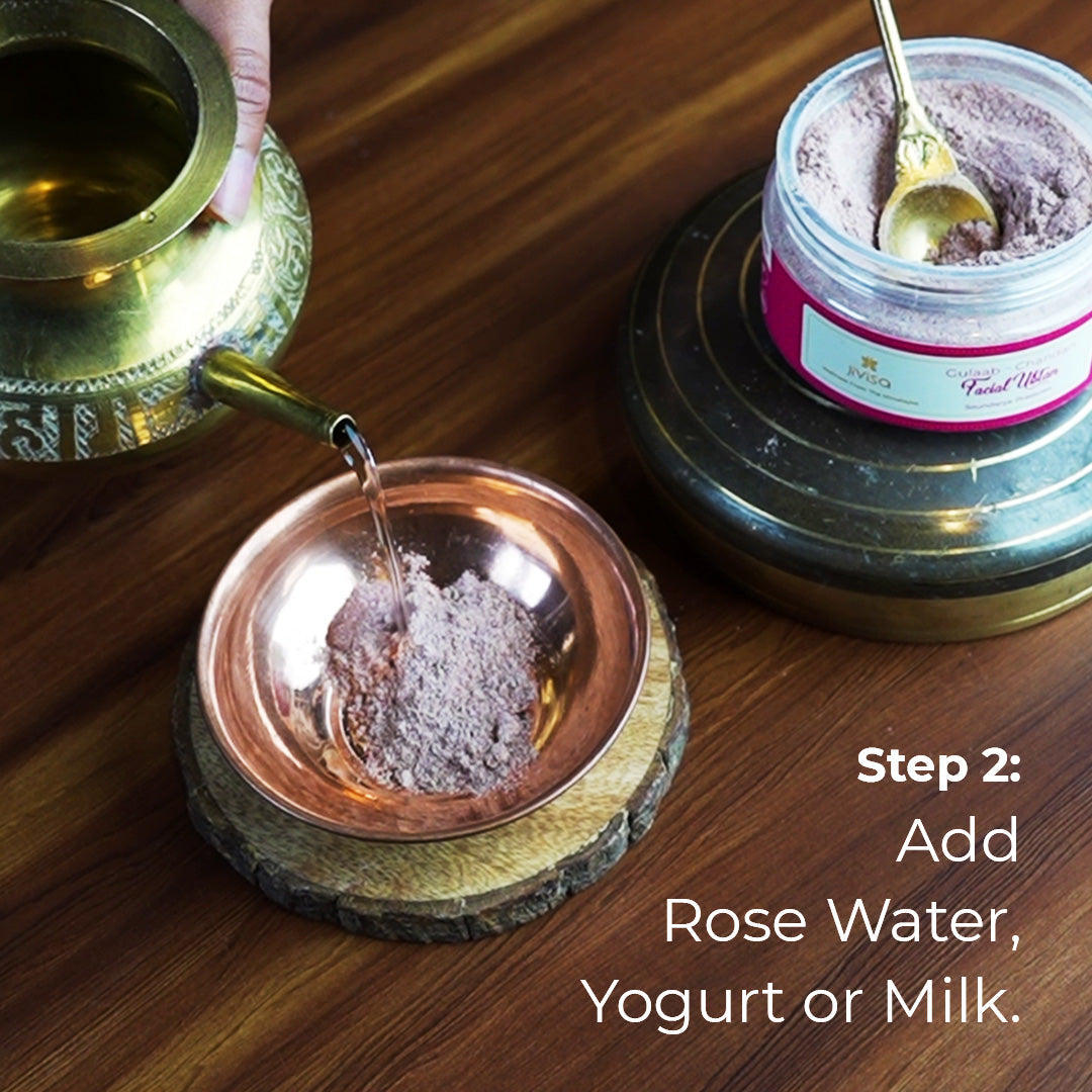 A small ornate brass pitcher is pouring a clear liquid likely a rose water into a copper bowl containing light brown powder identified as JiViSa Gulaab Chandan Facial Ubtan.
The text highlights instruction, 
Step 2: Add Rose Water, Yogurt or Milk
