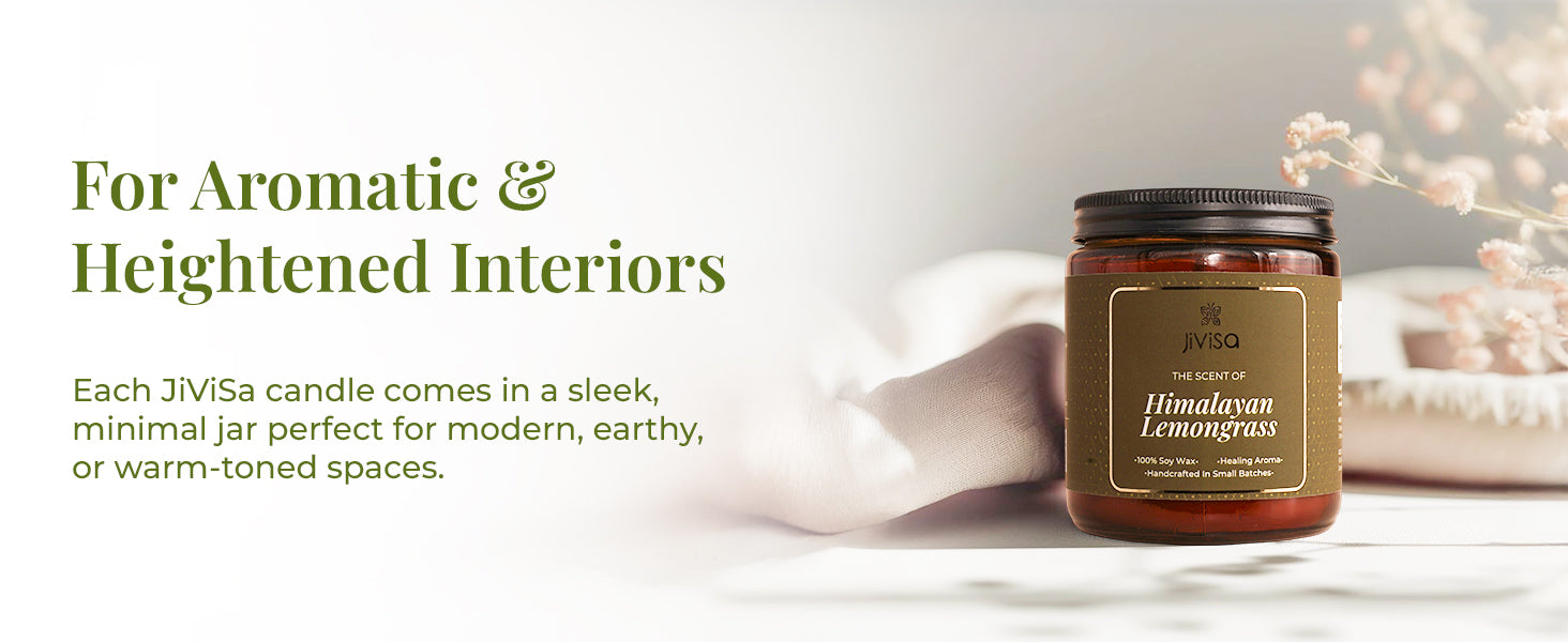 JiViSa Himalayan Lemongrass soy wax candle amber jar is displayed on a soft, neutral-toned surface with delicate pink flowers in the background. The text on the left reads: “For Aromatic & Heightened Interiors.” Below it, the description states: “Each JiViSa candle comes in a sleek, minimal jar perfect for modern, earthy, or warm-toned spaces.” The overall aesthetic is calm, warm, and minimal.