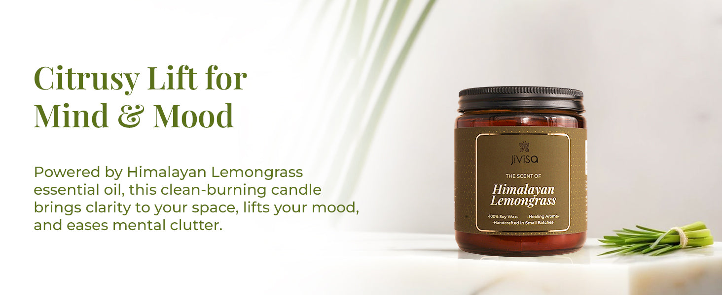 JiViSa Himalayan Lemongrass soy wax candle amber glass jar is positioned next to fresh lemongrass on a clean white surface with soft shadows and green foliage accents. The heading on the left reads: “Citrusy Lift for Mind & Mood.” Supporting text says: “Powered by Himalayan Lemongrass essential oil, this clean-burning candle brings clarity to your space, lifts your mood, and eases mental clutter.”
