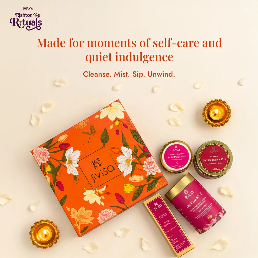 JiViSa Rose radiance gift set flat lay with orange floral box, rose tea tin, ubtan jar, candle and face mist surrounded by diyas and white petals. Made for moments of self care.