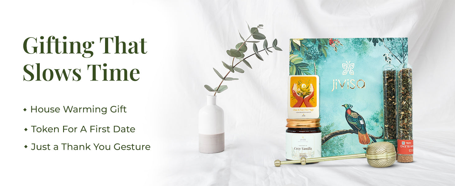 JiViSa Brew & Bliss Gift Box featuring a Cozy Vanilla candle in a glass jar, glow affirmation gift card, two herbal tea blends in glass tubes, and a brass infuser, arranged beside a nature-inspired green gift box and a ceramic vase with eucalyptus. Tagline on the left reads: “Gifting That Slows Time.” Followed by bullet points: House Warming Gift | Token For A First Date | Just a Thank You Gesture.