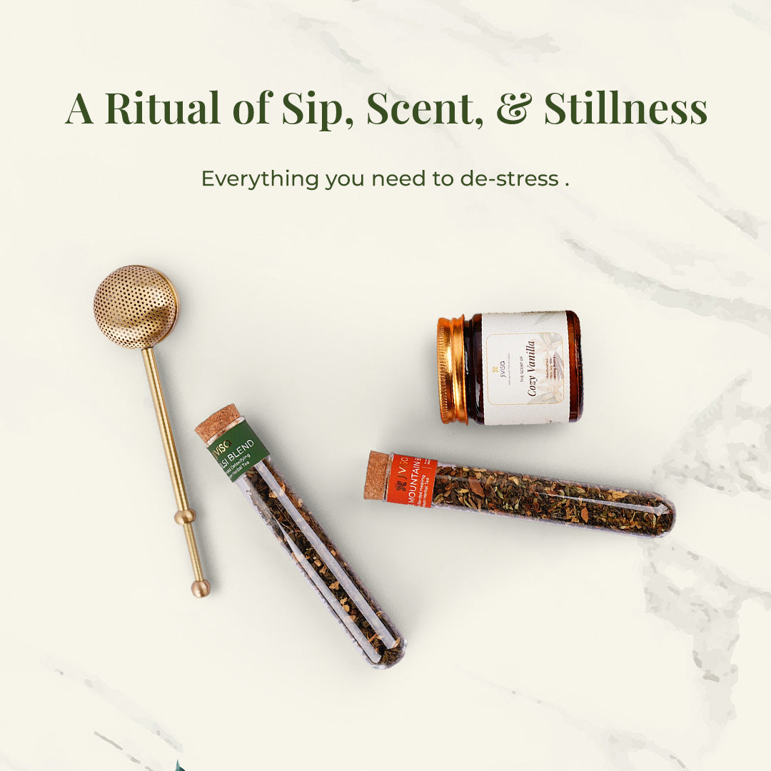 Flat lay of JiViSa Brew &amp; Bliss Gift Set products on a marble surface: a reusable brass tea infuser, Tulsi Blend tea, Mountain blend tea, and Cozy Vanilla aroma candle. Text reads: “A Ritual of Sip, Scent, &amp; Stillness” followed by the subtext &