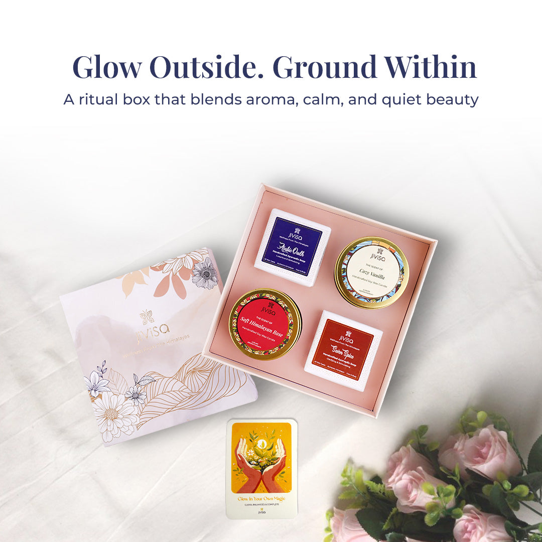 Text on image reads: &quot;Glow Outside. Ground Within&quot; – A ritual box that blends aroma, calm, and quiet beauty. A styled top-view of the open JiViSa Himalayan Ritual Soap &amp; Candle gift box revealing all four ritual products includes Royal Oudh &amp; Soft Himalayan Rose Candles, Seven Spice &amp; Arabic Oudh Soaps, alongside the illustrated &quot;Glow In Your Own Magic&quot; handwritten gift card. The setup is surrounded by soft roses and white fabric, evoking relaxation, aroma, and self-care.
