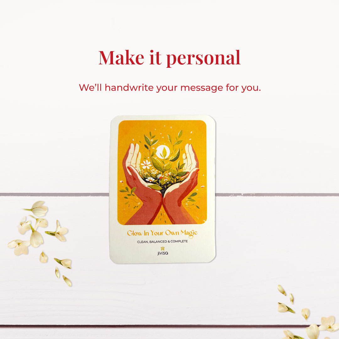 &quot;Make it personal – We’ll handwrite your message for you.&quot; A handwritten card with warm yellow and orange tones shows two hands holding blooming herbs with a glowing sun. Placed on a white wooden surface with jasmine flowers scattered around, the image emphasizes the personal, heartfelt gifting experience JiViSa offers.