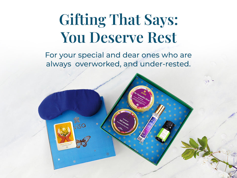 Flat lay of JiViSa Dreamscape Relaxation Gift Set opened on a marble surface. Inside are a navy eye mask, JiViSa Tranquility Blend tea tin, JiViSa Soft Lavender soy wax candle, and a JiViSa Raina Slumber pillow mist, JiViSa Palmorosa essential oil, and a Handwritten message card. Tagline reads: "Gifting That Says: You Deserve Rest." Supporting text: For your special and dear ones who are always overworked and under-rested.

