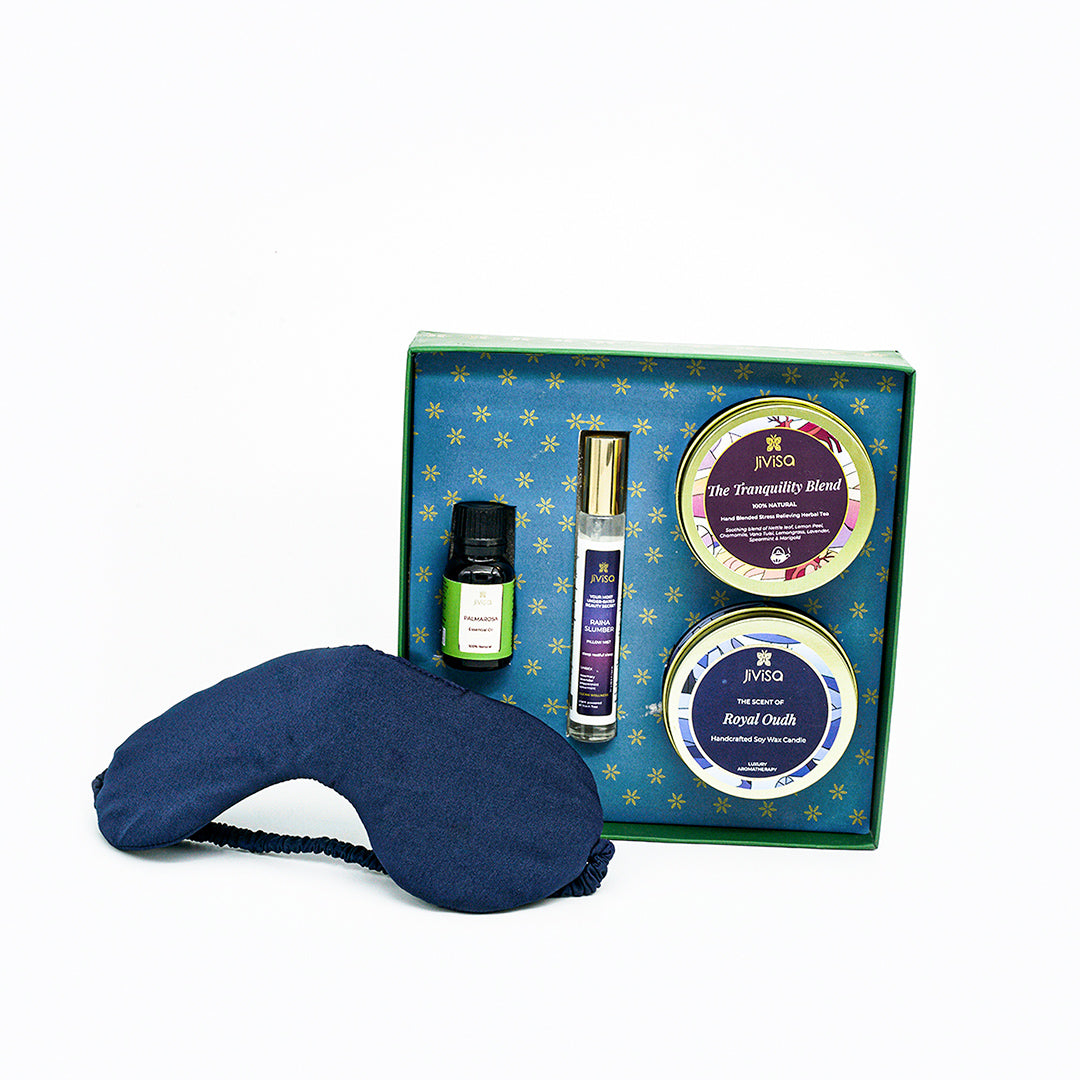 Front View of JiViSa-Dreamscape Relaxation Gift Set featuring the JiViSa Tranquility Blend Stress Relief Herbal Tea, the Royal Oudh Premium Soy Wax Candle, a bottle of Palmarosa Essential Oil, the soothing Raina Slumber Pillow Mist and a soft blue eye mask.