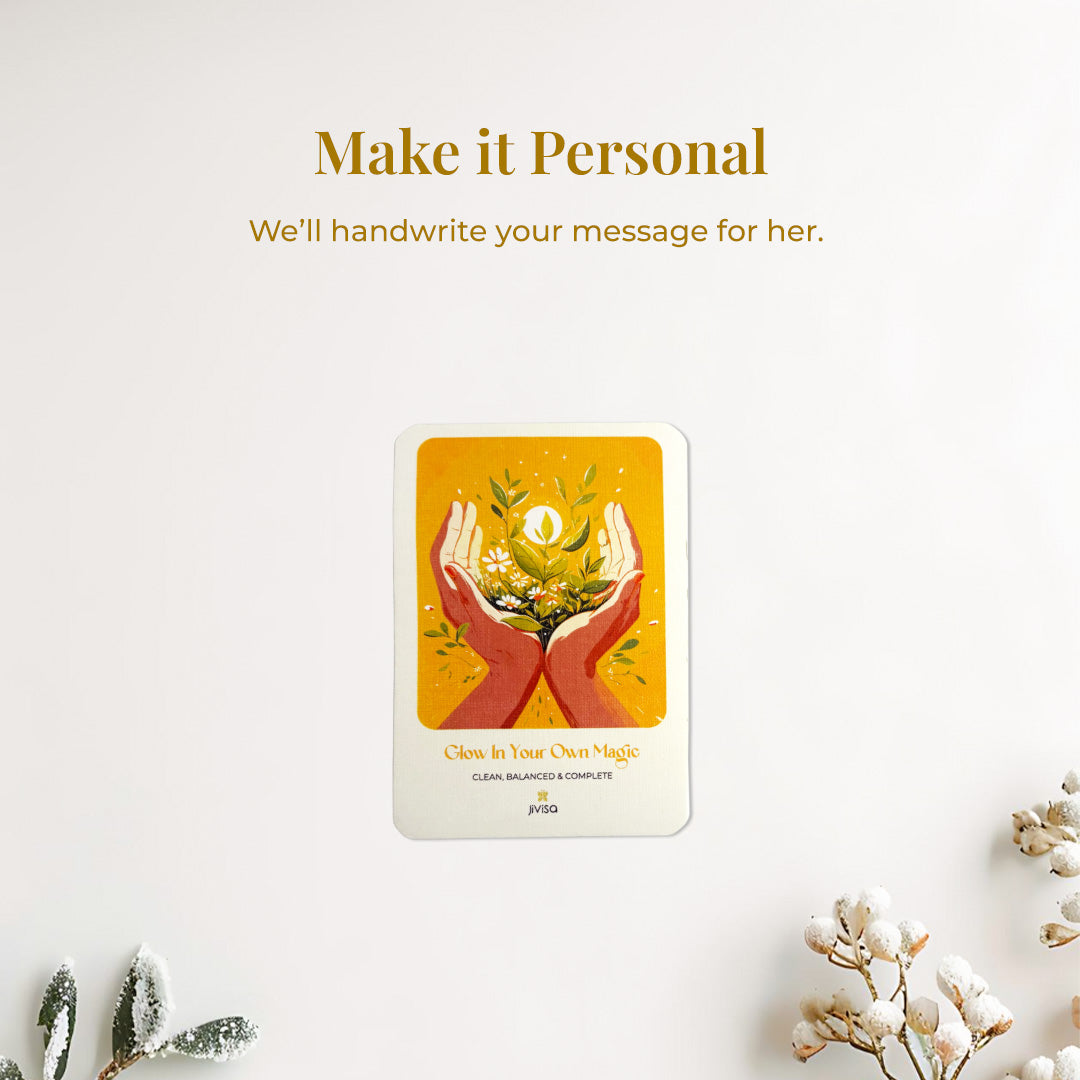 &quot;Make it personal – We’ll handwrite your message for you.&quot; A handwritten card with warm yellow and orange tones shows two hands holding blooming herbs with a glowing sun. Placed on a snow surface with white flowers scattered around, the image emphasizes the personal, heartfelt gifting experience JiViSa offers.
