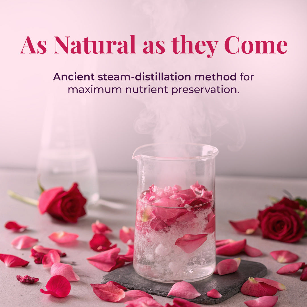 A glass beaker filled with pink rose petals and water steam, representing the ancient steam-distillation method. Scattered rose petals and a fresh rose are seen on the table. Text on the image reads: &
