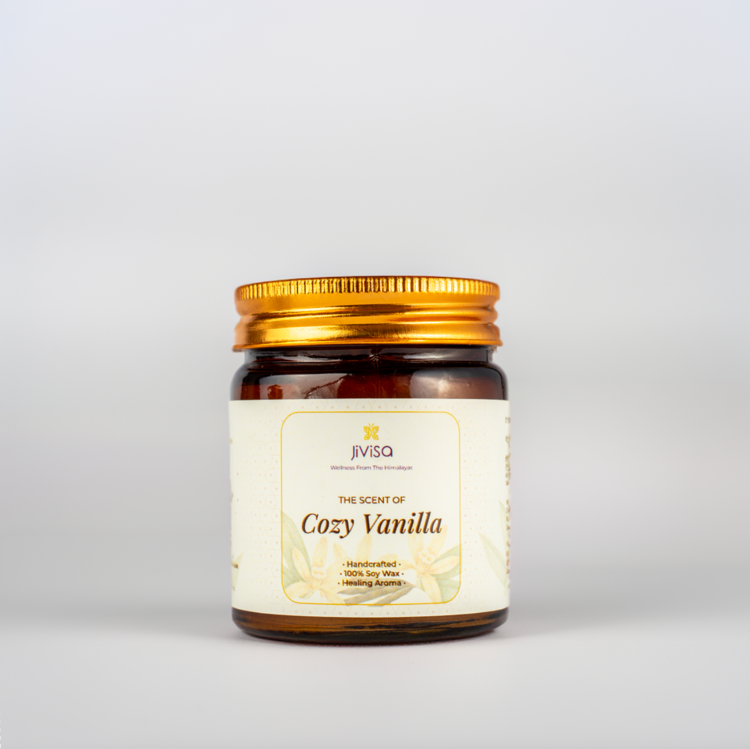 JiViSa Cozy Vanilla soy wax candle in a glossy amber glass jar with a golden lid, placed against a white background. The label reads: &quot;JiViSa – Wellness From The Himalayas – The Scent of Cozy Vanilla – Handcrafted • 100% Soy Wax • Healing Aroma.&quot;