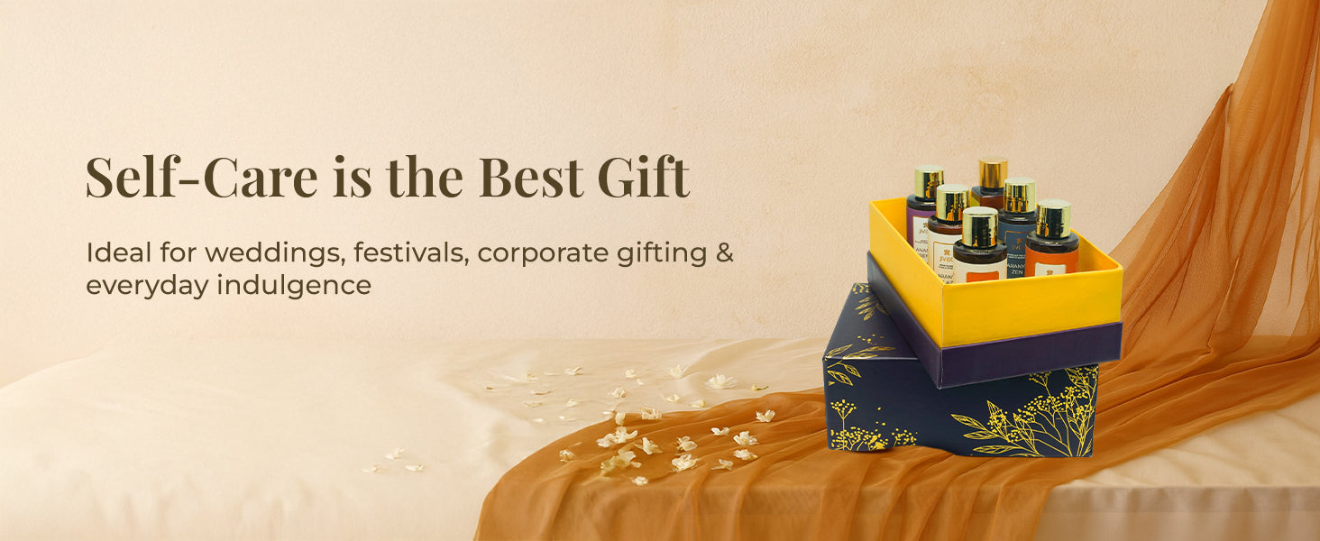 JiViSa Soulful Self-Care gift box stacked on a beige surface, draped with a flowing, sheer golden-brown cloth. The top box is yellow with six small bottles inside, while the bottom box is a deep purple with a gold floral pattern. The text on the image reads, "Self-Care is the Best Gift," followed by a description: "Ideal for weddings, festivals, corporate gifting & everyday indulgence."